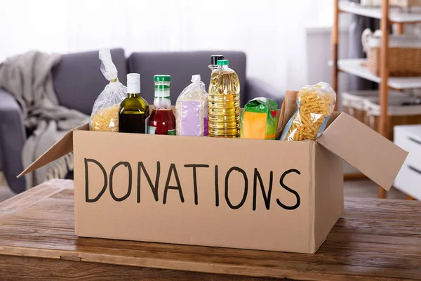Various Food Items In Donation Box On Wooden Table