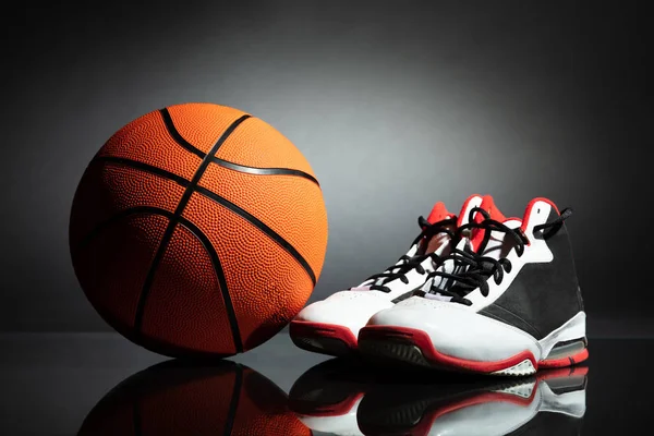 Paar Sportschuhe Und Basketball Auf Dem Schreibtisch Vor Schwarzem Hintergrund — Stockfoto