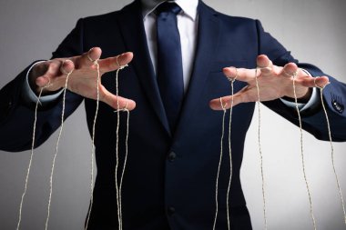 Erkeğin Eli, parmakları gri arkaplana bağlı kuklayı kontrol eder.