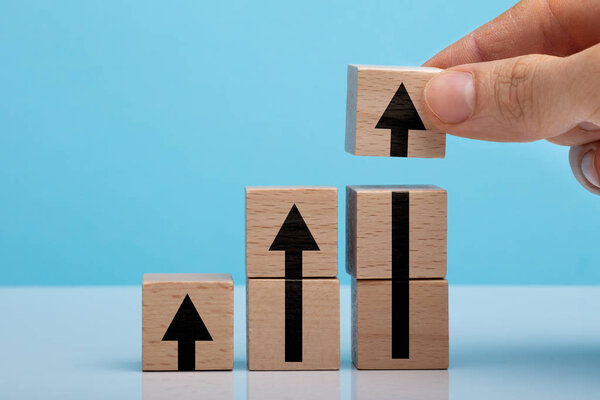 Man's Hand Arrow Sign Wooden Block On White Table Against Blue Backdrop