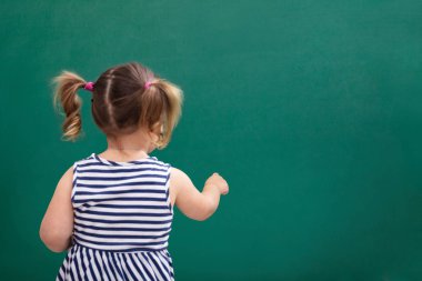 Yeşil kara tahta üzerinde bir kız öğrencinin yazma tebeşir ile arkadan görünüş