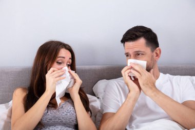 Yatakta oturup, yatak odasında burnunu silen genç bir çift.