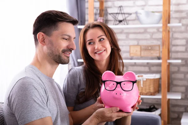 笑顔若いカップルがソファに座っているピンクの貯金箱を保持 — ストック写真