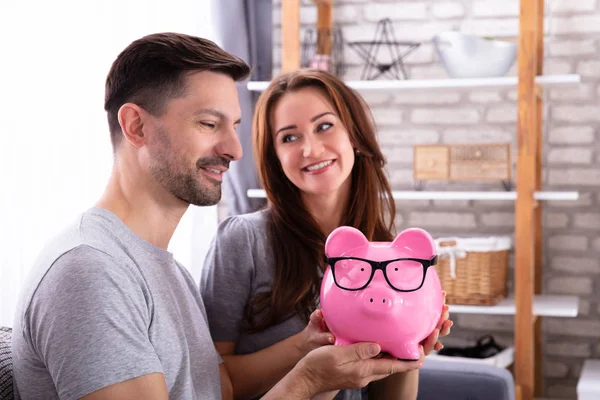 Sonriente Pareja Joven Sentada Sofá Sosteniendo Pink Piggybank —  Fotos de Stock