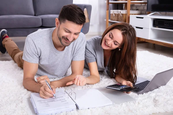 Sorrindo Jovem Casal Deitado Tapete Calculando Fatura Com Calculadora — Fotografia de Stock