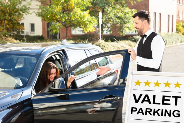Happy Male Valet Opening Car Door Near Valet Parking Sign