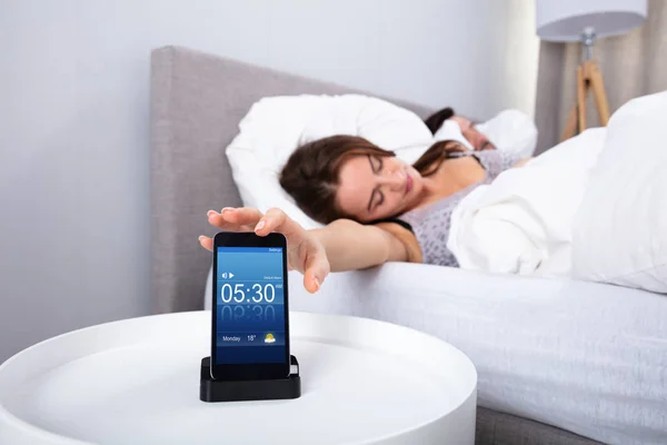 Young Woman Sleeping Near Alarm Set On Mobile Phone In Bedroom