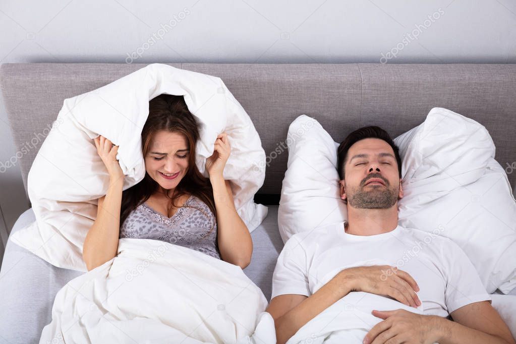 An Elevated View Of Young Woman Covering Her Ears With Pillow While Man Snoring