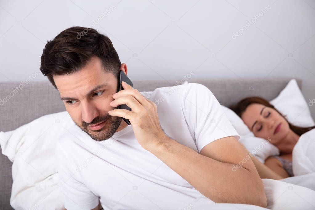 Close-up Of Man Talking Secretly On Cellphone While His Wife Sleeping