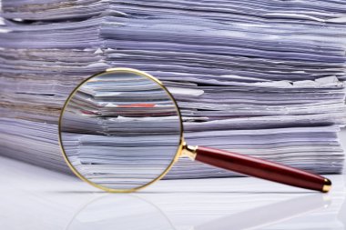 Yığılmış kağıt dosyalarının arkaplanındaki büyüteçin yakın plan görüntüsü