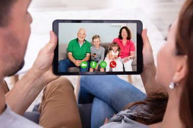 Koltukta oturup mutlu aileleriyle dijital tablet kullanarak konferans yapan çift.