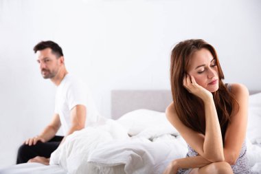 Depresyondaki kadının kocasının önünde yatağında otururken yakın plan fotoğrafı.