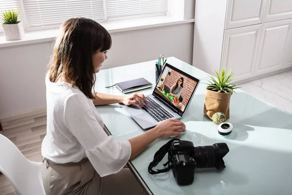 Businesswoman Video Conferencing Using Laptop With DSLR Camera On Desk At Workplace