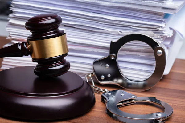 Gavel 'in yakın çekimi ve ahşap masa üzerine istiflenmiş kağıdın yanındaki kelepçeler.