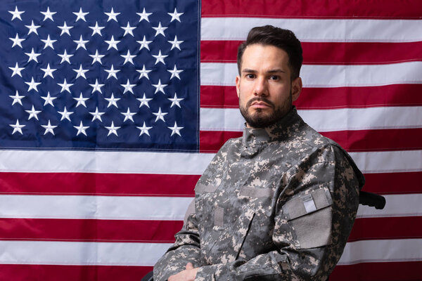 Side View Of Veteran Sitting In Wheelchair In Front Of An American Flag