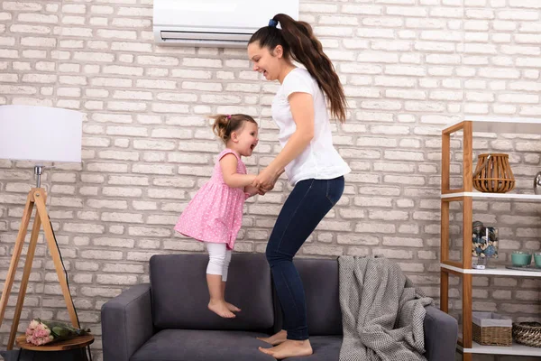 Happy Mother Daughter Holding Hands Jumping Sofa Together — стоковое фото
