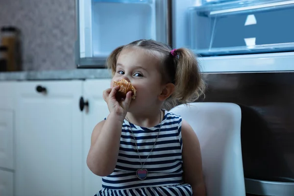Aranyos Kislány Eszik Cupcake Nyitott Hűtőszekrény Konyha Előtt Ülve — Stock Fotó