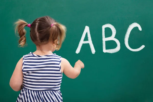 グリーンボードにAbcアルファベットを書く女子高生の背面図 — ストック写真