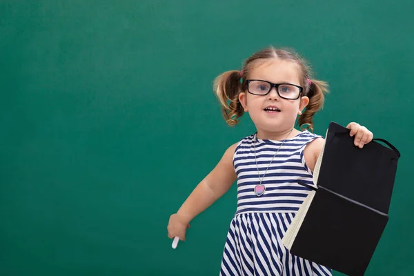 Schattig Klein Meisje Staande Voor Schoolbord Holding Book — Stockfoto