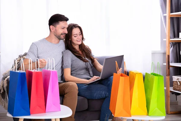 微笑的年轻情侣购物在笔记本电脑附近五颜六色的购物袋 — 图库照片