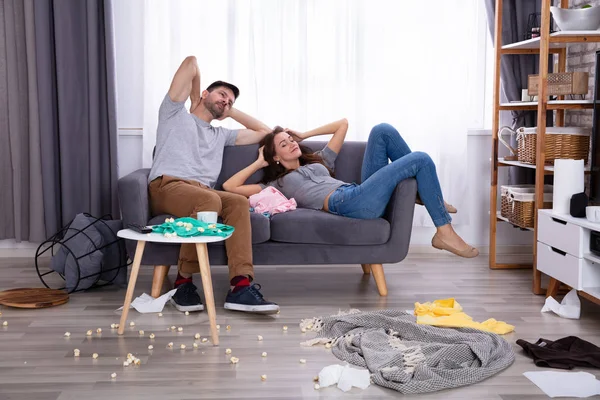 Smiling Couple Relaxing On Sofa In Messy Living Room At Home