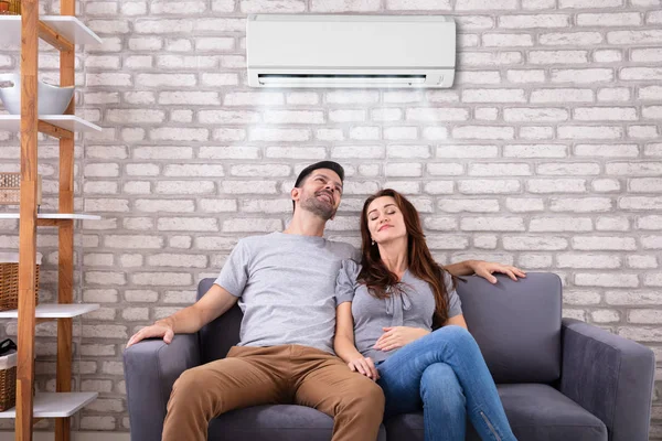 Happy Young Couple Sitting Air Conditioner Couch Home — Stock Photo, Image