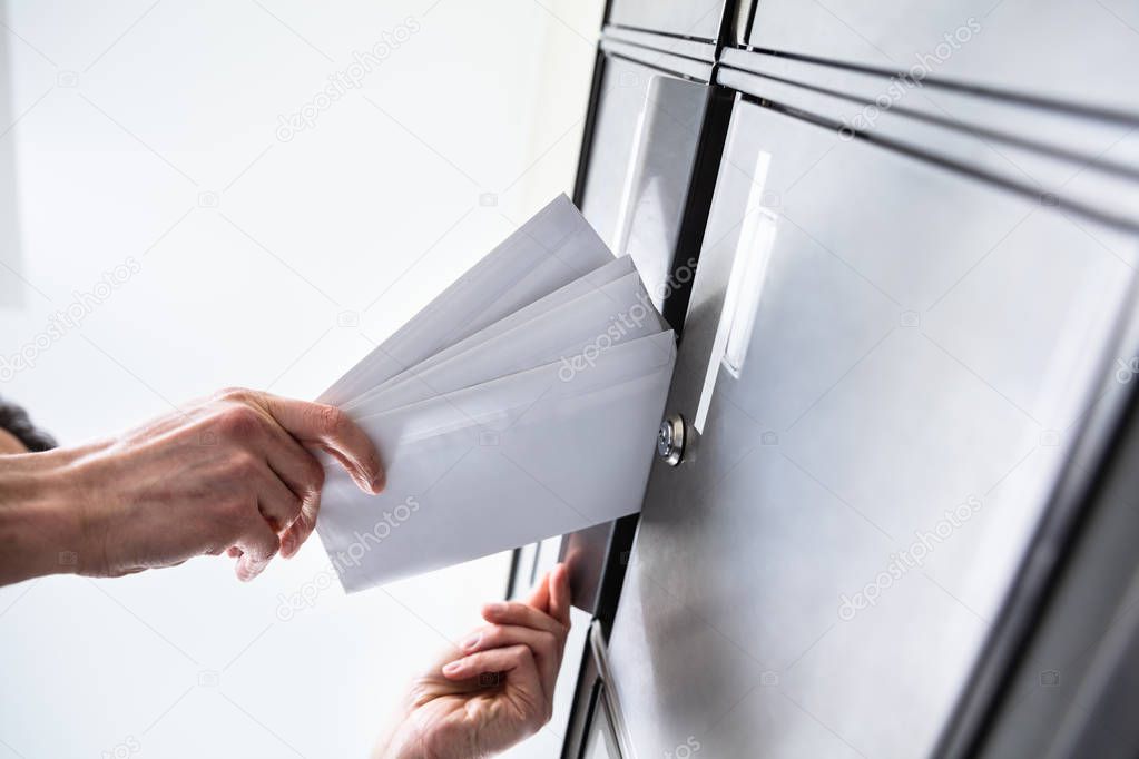 Low Angle View Of Person's Hand Inserting Envelopes In Mailbox