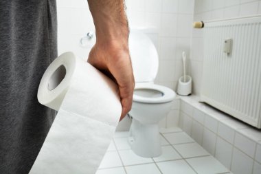 Man Suffers From Diarrhea Holding Tissue Paper Roll Standing In Front Of Toilet Bowl clipart