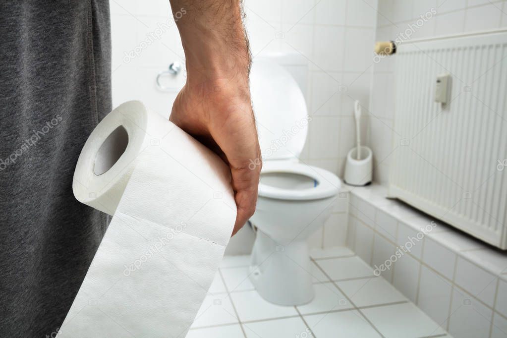 Man Suffers From Diarrhea Holding Tissue Paper Roll Standing In Front Of Toilet Bowl