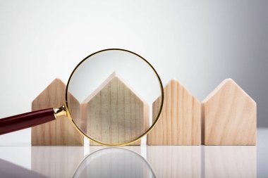Magnifying Glass In Front Of Wooden House Model Arranged In A Row clipart