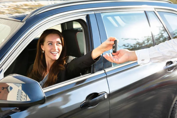 微笑的年轻女子坐在车里 给汽车钥匙给男性的手 — 图库照片