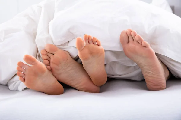 Close-up Of Couple\'s Bare Feet Under White Blanket