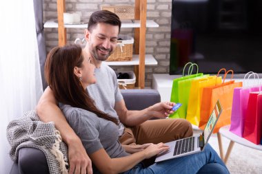 On laptop online alışveriş sırasında kredi kartı kullanarak mutlu çift yan görünümü