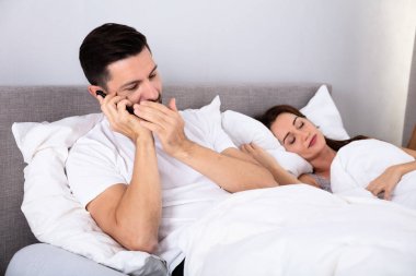 Genç adam, karısından başka akıllı telefonda konuşuyor. Yatak odasında uyuyor.