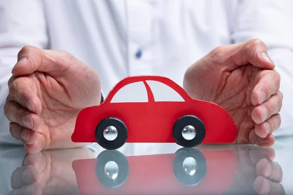 Geschäftsmann Schützt Rotes Spielzeugauto Auf Reflektierendem Schreibtisch — Stockfoto