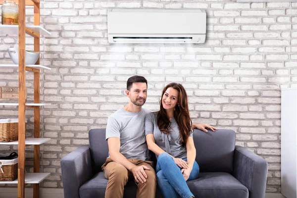 Happy Young Couple Sitting Air Conditioner Couch Home — Stok Foto