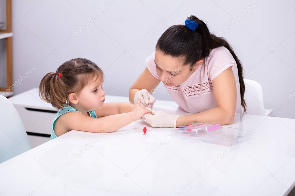 Young Mother Cutting Her Daughter Finger Nails By Using Electronic Nail Trimmer