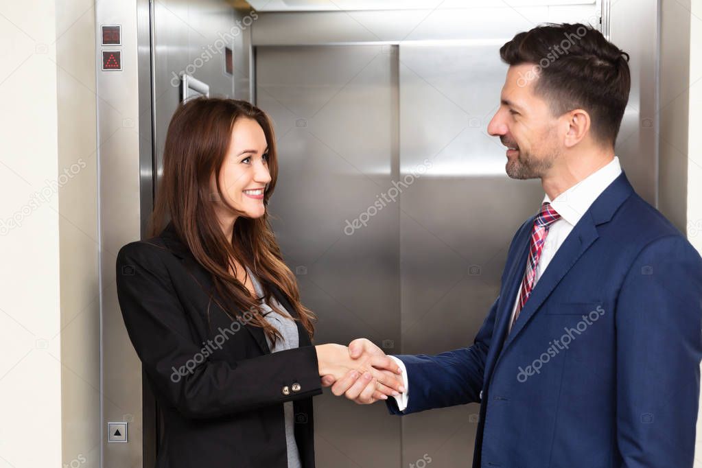 Smiling Young Businessman And Businessman Shaking Hands Near Elevator