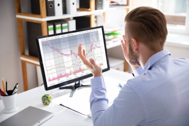 Umutsuz işadamı monitörler üzerinde masa danışmanlık grafikleri otururken mali kayıplar ile karşı karşıya