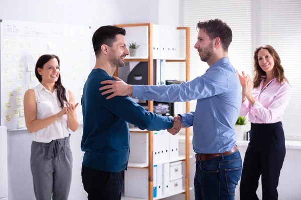 当其他同事在办公室里拍手叫好时 两个快乐的舞伴握手 — 图库照片