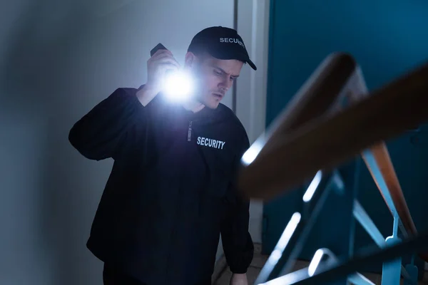 男性保安站在楼梯上手持手电筒的侧视图 — 图库照片