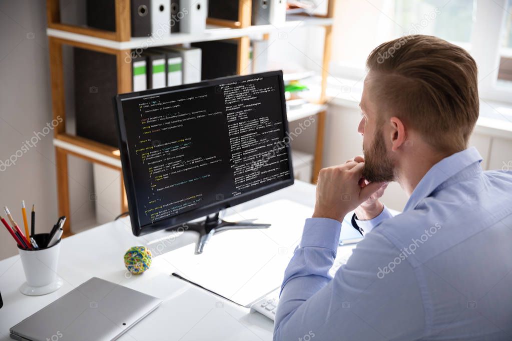 Computer programmer writing program code on computer in office 