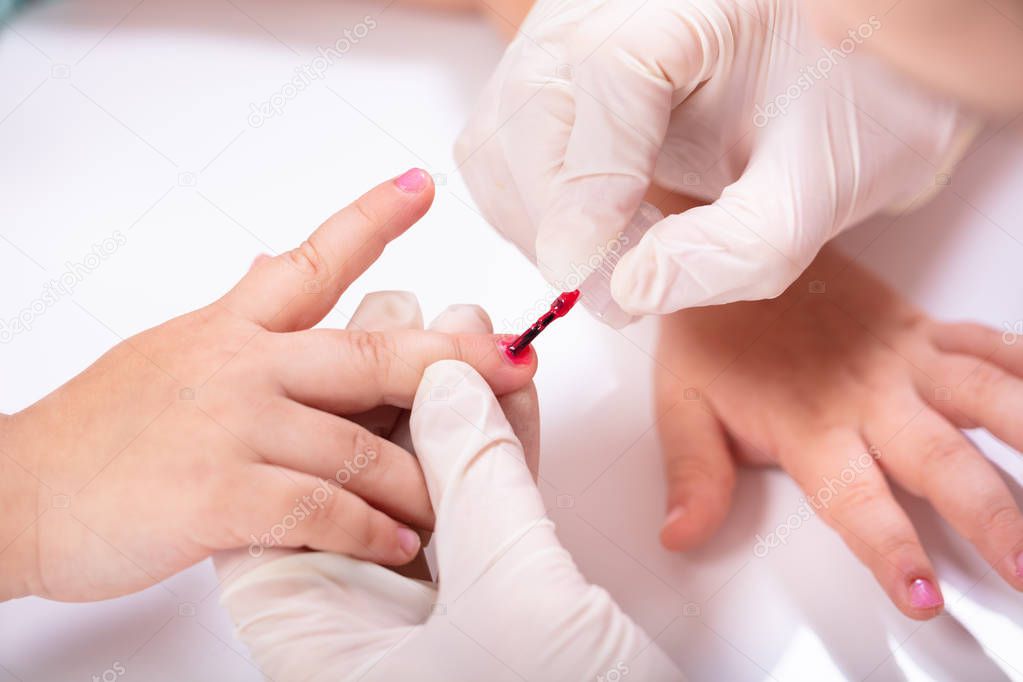 Close-up Of Beautician's Hand Applying Nail Polish To Girl's Nails At Beauty Salon