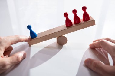 Masanın üzerinde tahtadan testere üzerinde dengelenmiş kırmızı ve yeşil piyon figürleri.