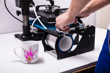Man printing on coffee mugs in workshop clipart