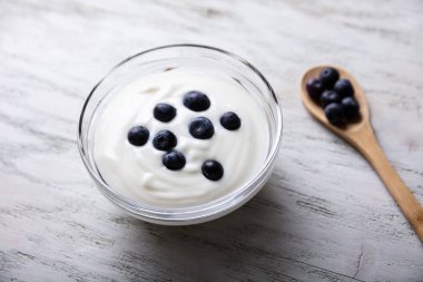 Masanın üzerinde yabanmersinli beyaz yoğurt ve ahşap kaşık.
