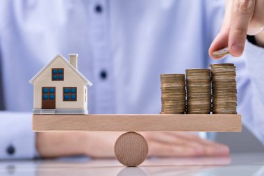 Adamın eli bozuk paraları yığının üstüne koyuyor ve tahterevallinin üzerine mankenler koyuyor.