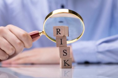 Büyüteç Camı tutan işadamı'nın el önündeki Risk sözcüğü ile ahşap bloklar Close-Up