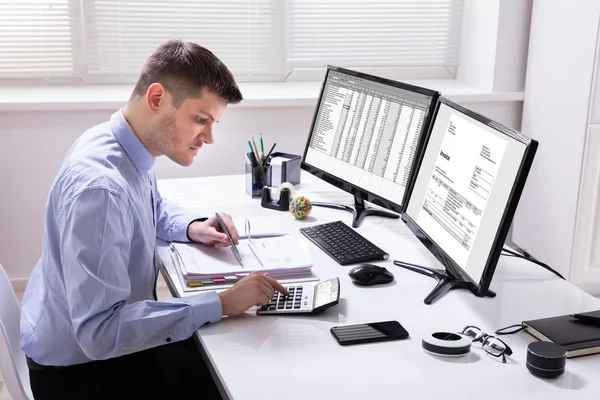 若いビジネスマン計算機を使ってコンピュータ画面上の請求書を計算する — ストック写真