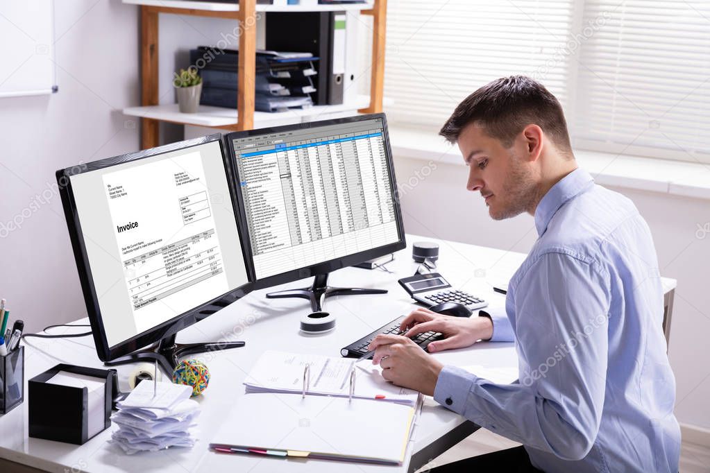 Side View Of Businessman's Hand Calculating Invoice At Workplace